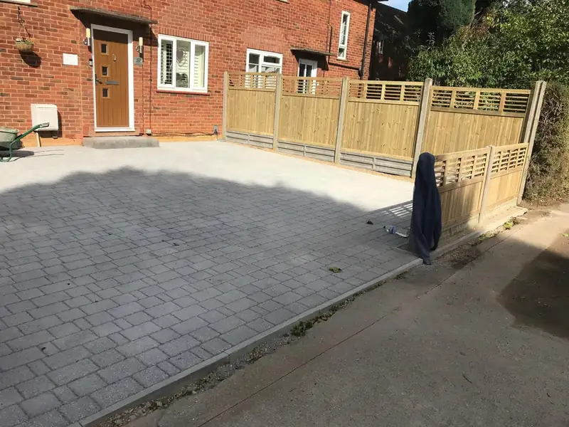 A block paved drive in front of a brick house with a new fence