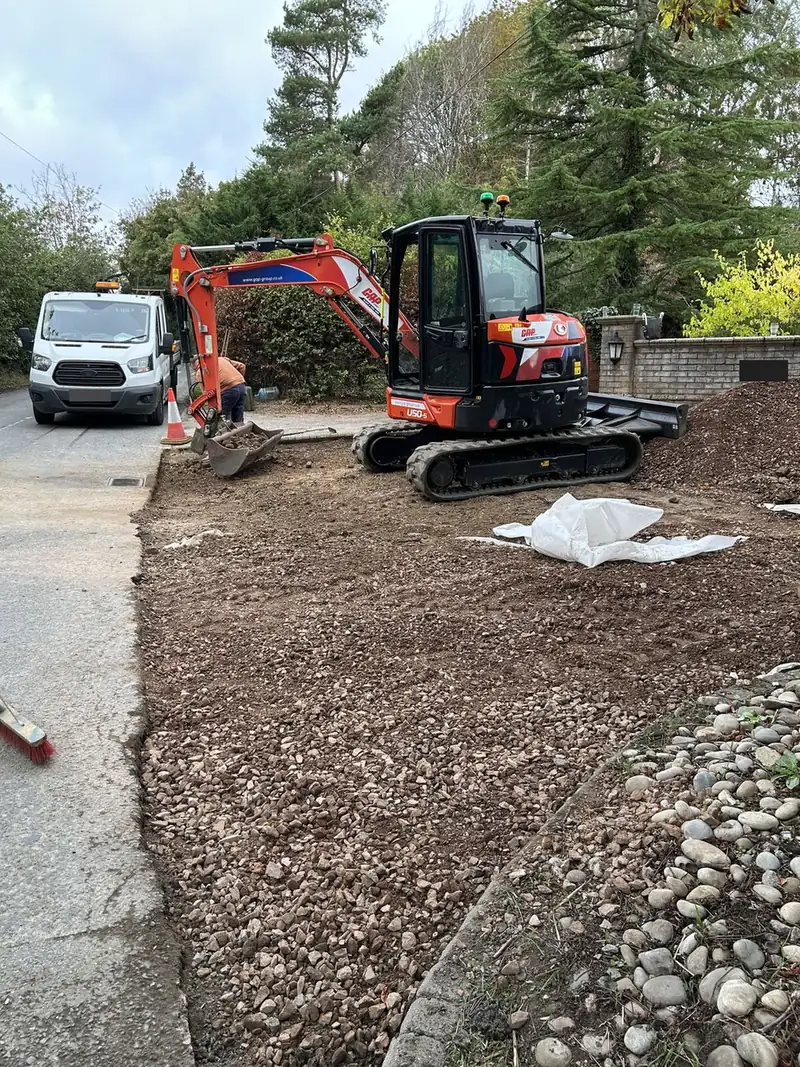 Tracked mini digger beside a pile of sub-base stone on a driveway