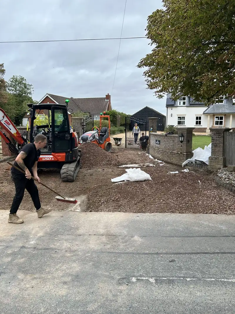Groundworks team grading sub-base stone with a mini digger at a driveway entrance