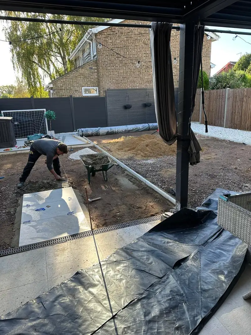 Laying a porcelain patio on a prepared base, with a wheelbarrow of mortar beside the work