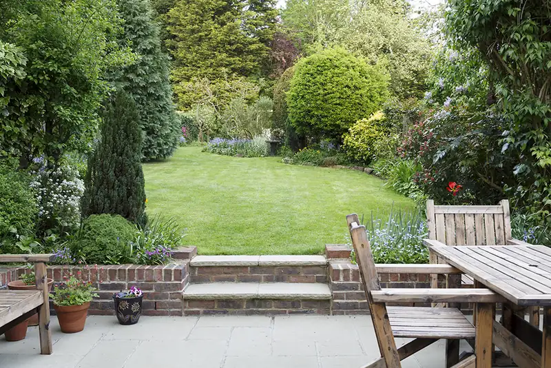 Lawn and brick steps leading up to a paved seating area