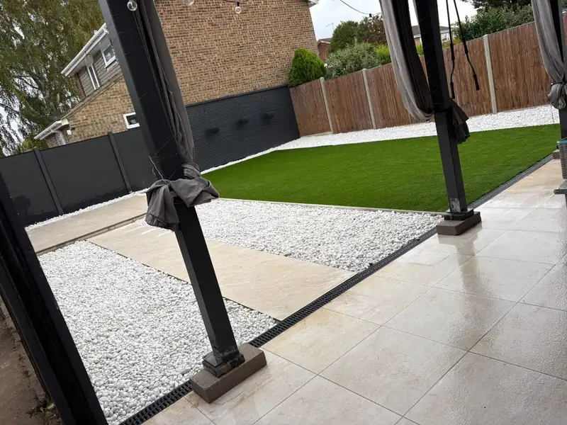 Porcelain patio with a stepping stone path through white gravel, a lawn and a dark fence