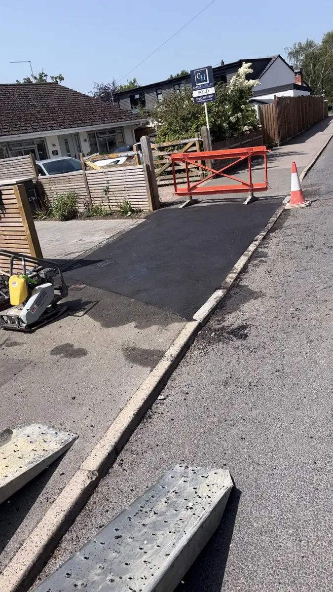 A new tarmac access beside the road, with a plate compactor and a barrier