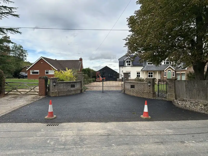 Completed tarmac driveway with two traffic cones in front of gates and a house