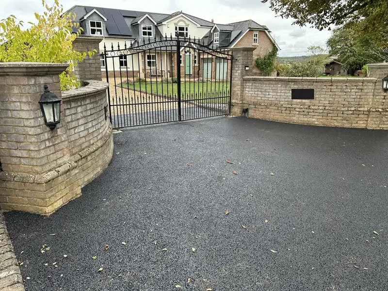 New tarmac driveway curving past a brick wall to black metal gates