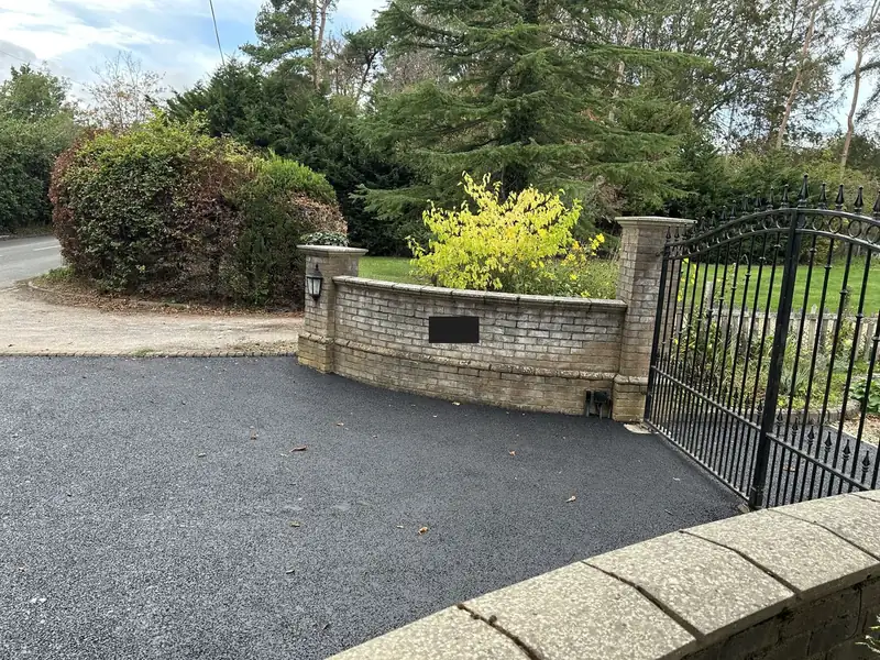 Fresh tarmac driveway beside a curved brick wall and an open gate