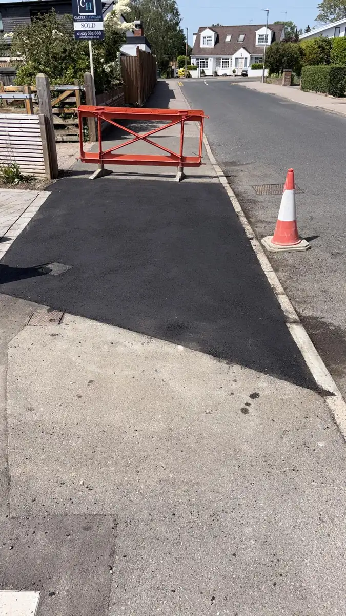 A new tarmac dropped kerb access with a barrier and a cone