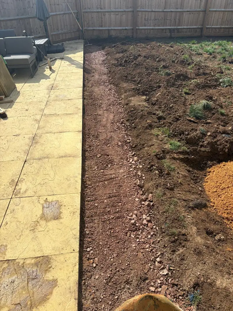 Prepared soil bed running alongside a patio before turf goes down