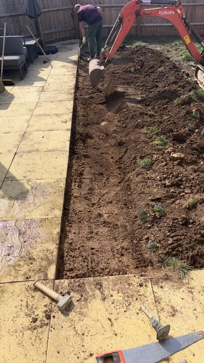 A mini digger preparing soil for turf beside a paved patio
