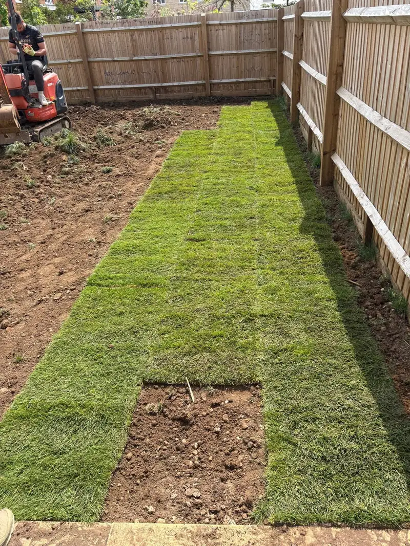 Turf being laid in rows along a timber fence